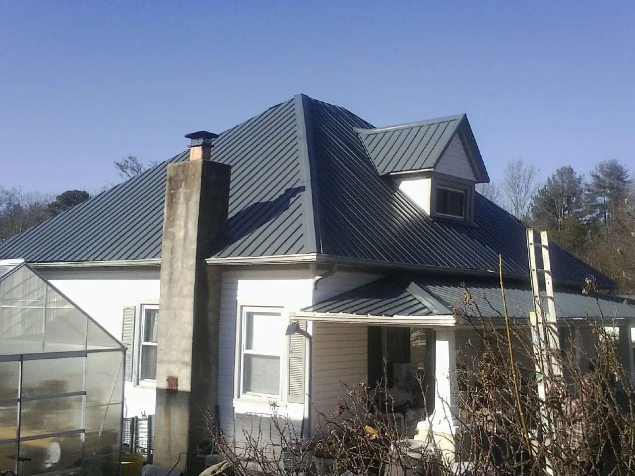 Dark blue standing seam metal roof on a white farmhouse with dormer — Slate & Tile Roof Repair by Roofing Brothers in Fitchburg