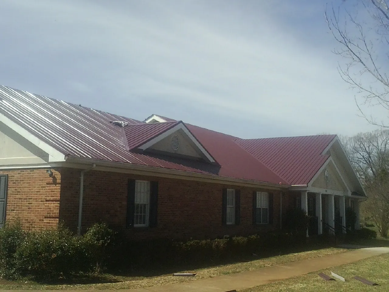 Red metal roof with gabled entries on a long brick building, from a Hail Damage Roof Repair job in Fitchburg