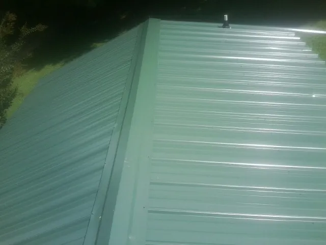 New green metal panels meeting at the ridge of a roof — Flat Roof Repair work by our crew in Fitchburg