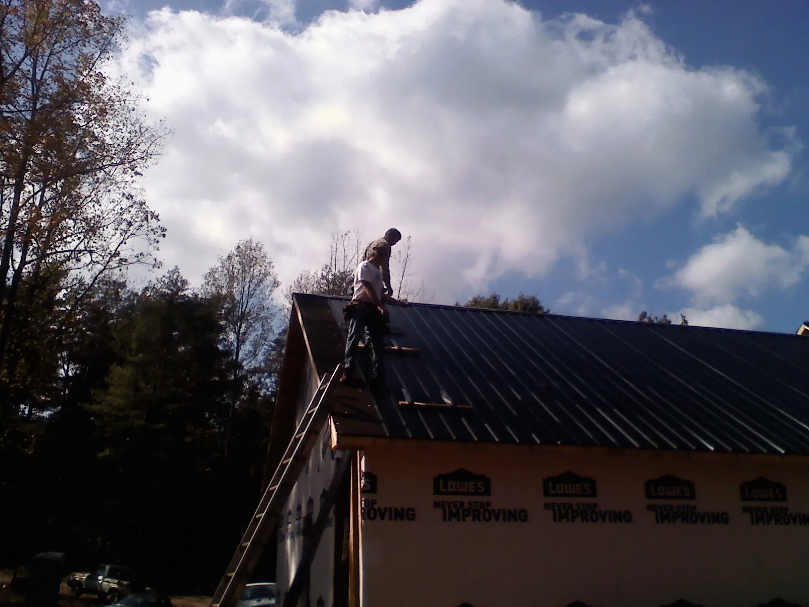 Roofer fastening dark metal panels high against a cloudy sky, from a Roof Inspection job in Fitchburg