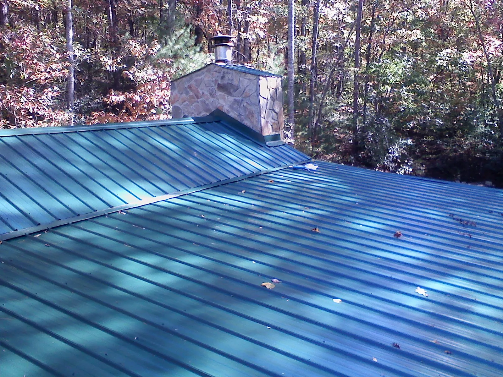 New green metal roof and stone chimney surrounded by autumn woods in Fitchburg