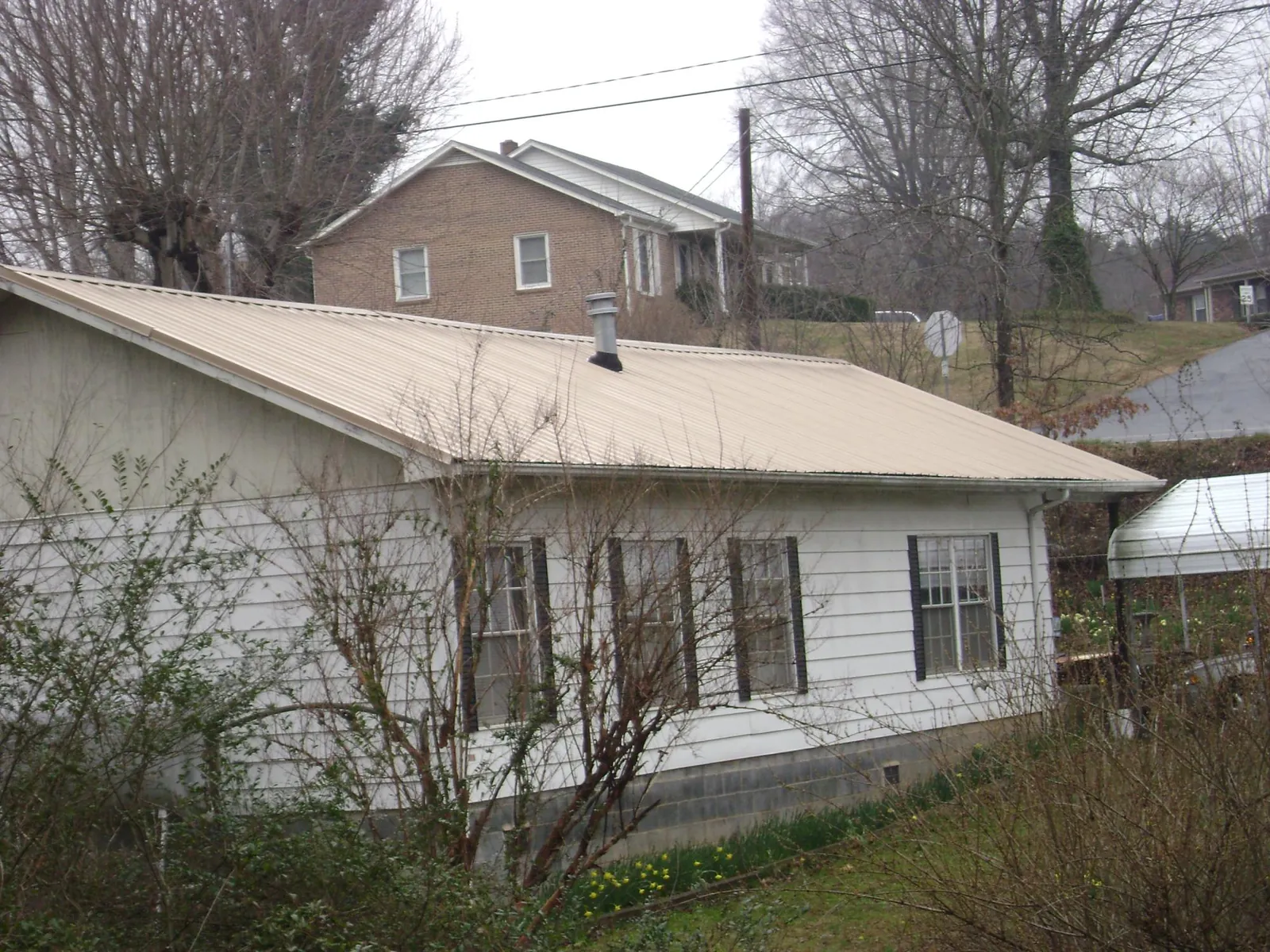 Tan metal roof on a white sided house set into a hillside — Commercial Roofing by Roofing Brothers in Fitchburg