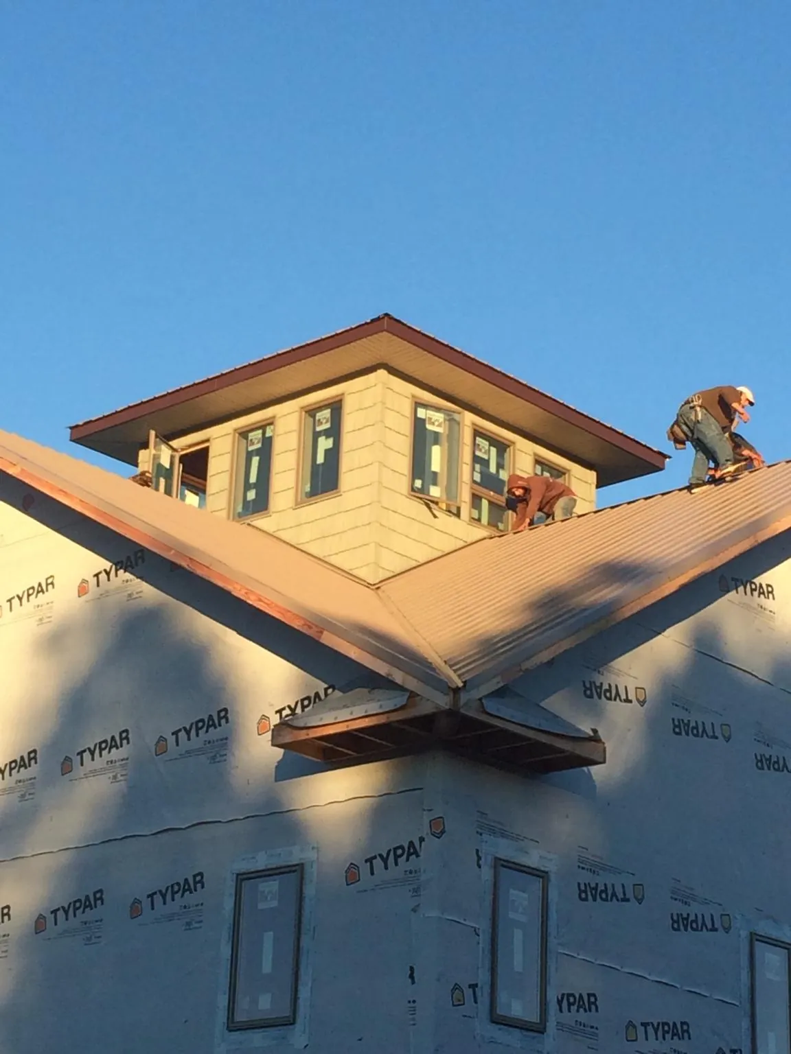 Roofers working around a rooftop cupola on a new metal roof at sunset — Roof Waterproofing in Fitchburg by Roofing Brothers